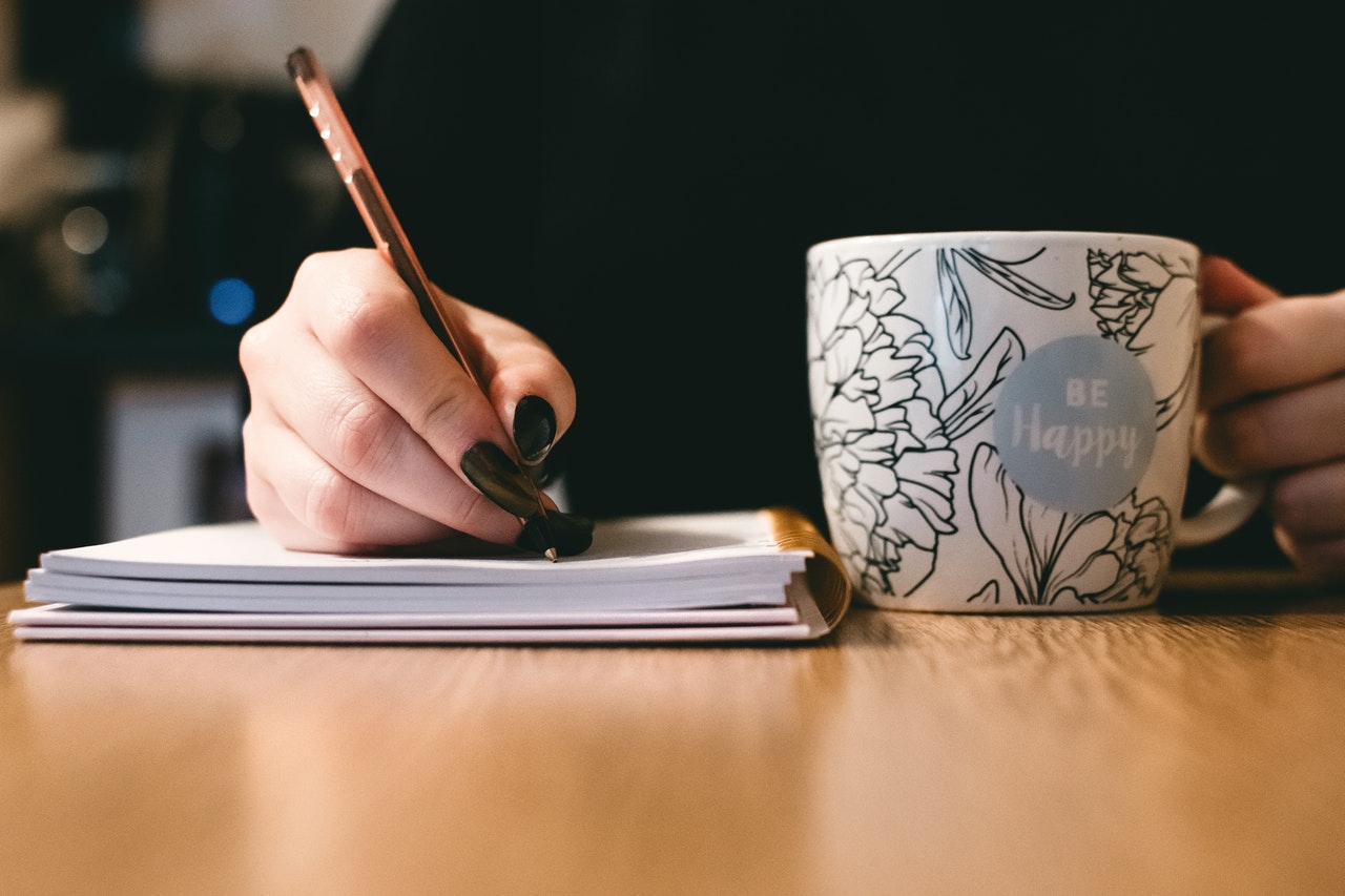 A shot of a girl taking notes with a coffee mug in her left hand